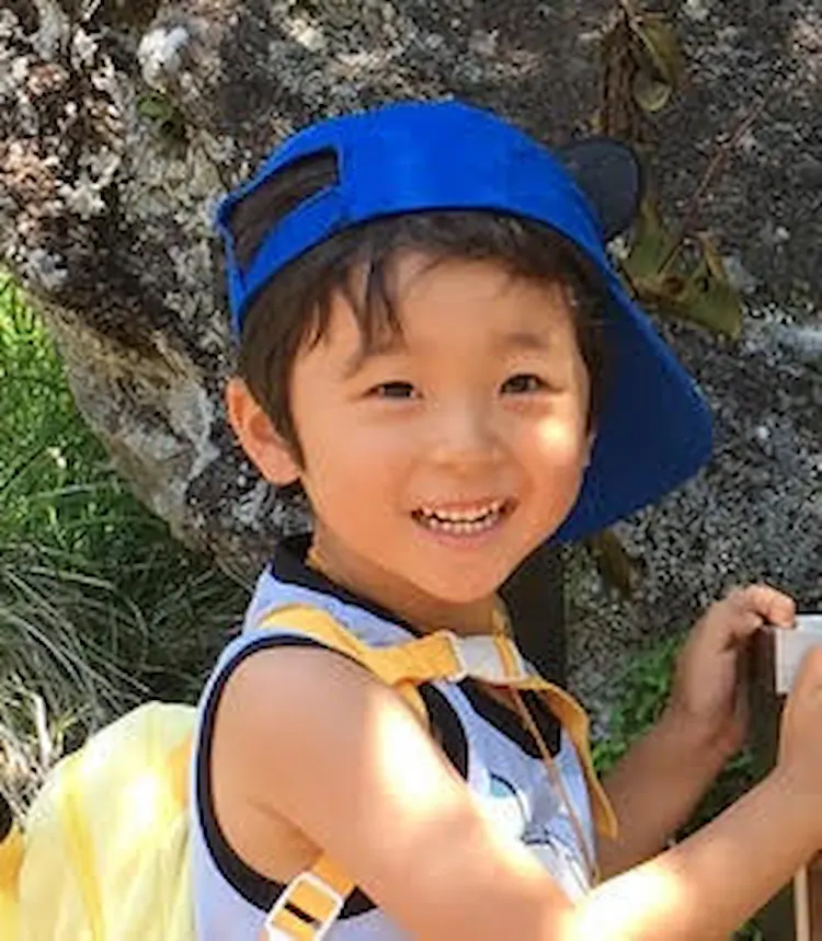 A little boy, with a blue baseball cap and a backpack.