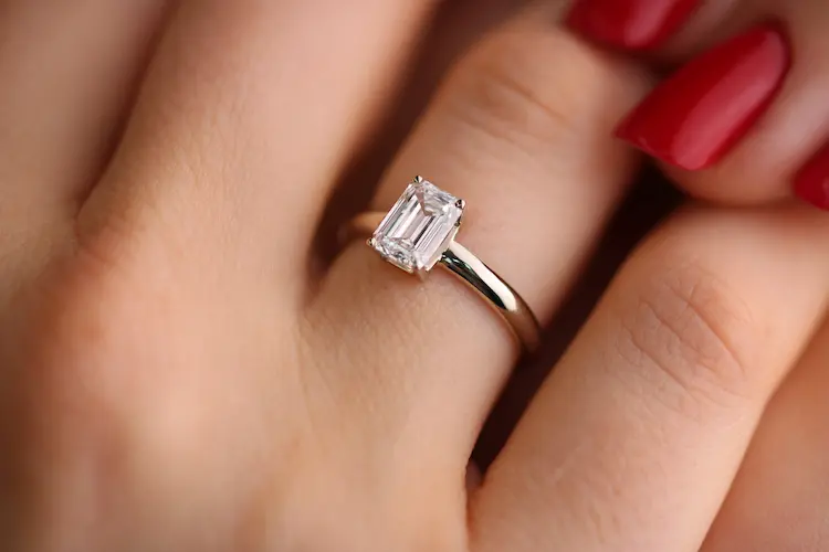 A colorless emerald cut memorial diamond ring on a woman's finger.