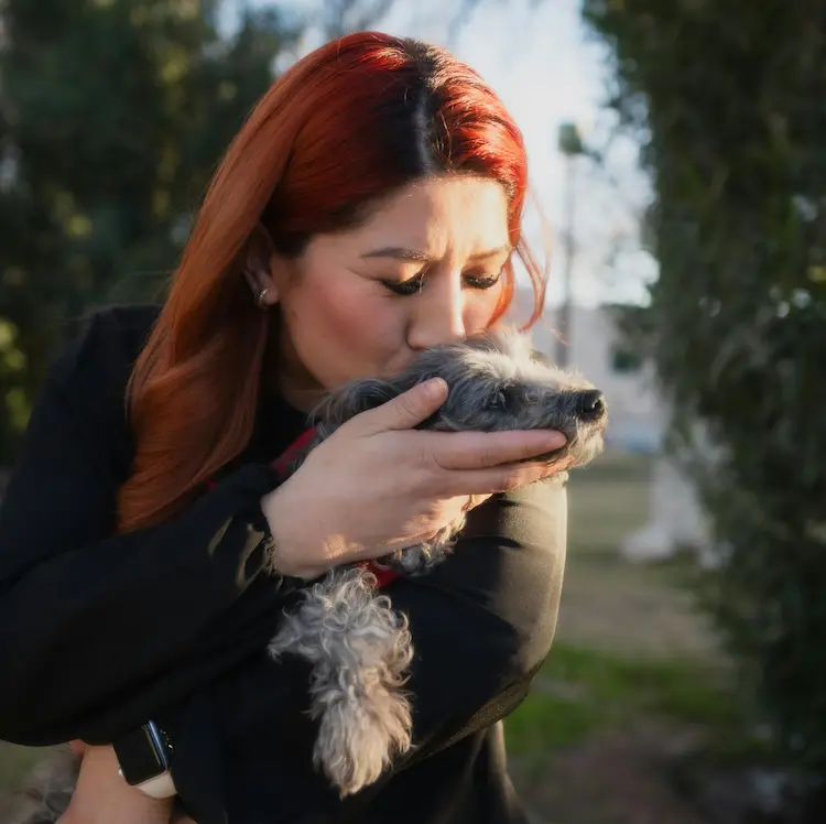 A woman holding a dog and kissing its head.