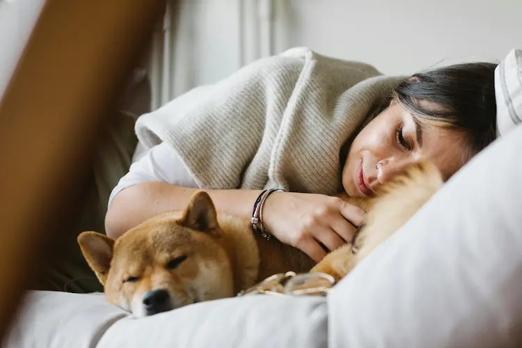 A woman and her dog, laying down together on a bed.