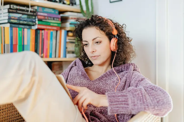 A woman, listening to music on headphones and reading.