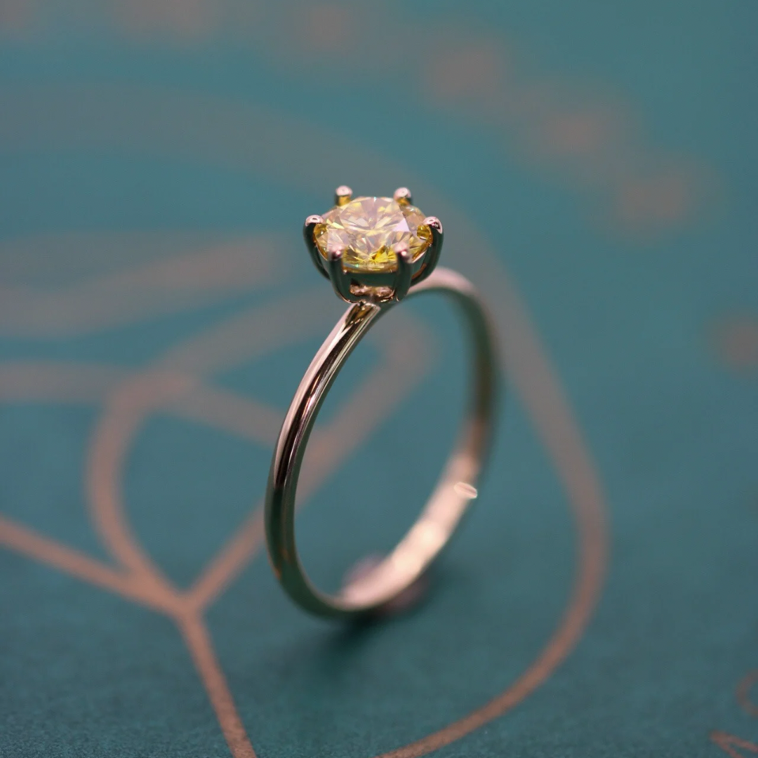 Yellow round cremation diamond set in a yellow gold ring band on a green background.