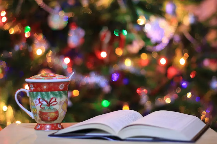 A cup and an open book by a christmas tree.