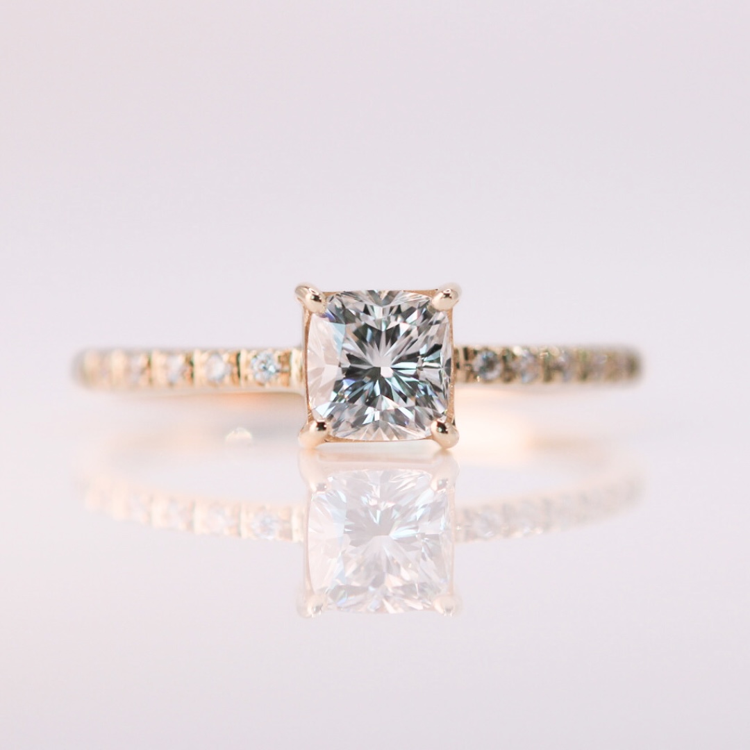 Colorless cushion cut diamond set in a yellow gold ring band, the band lined with small diamonds.