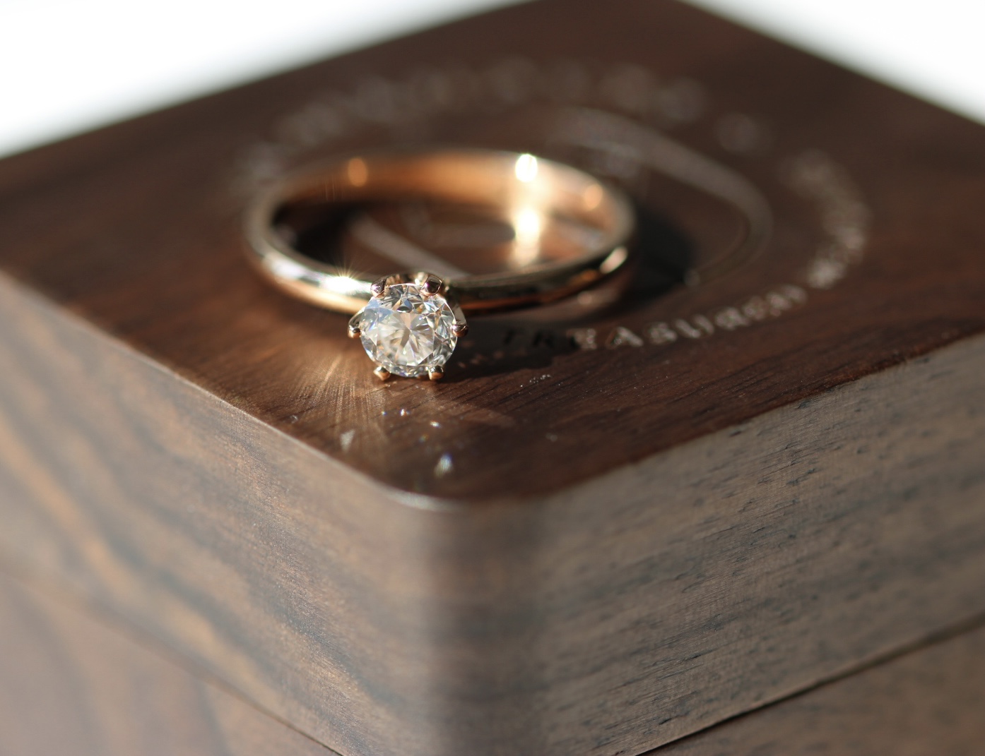 Colorless round memorial diamond set in a rose gold ring band, set on top of a brown wood ring box.