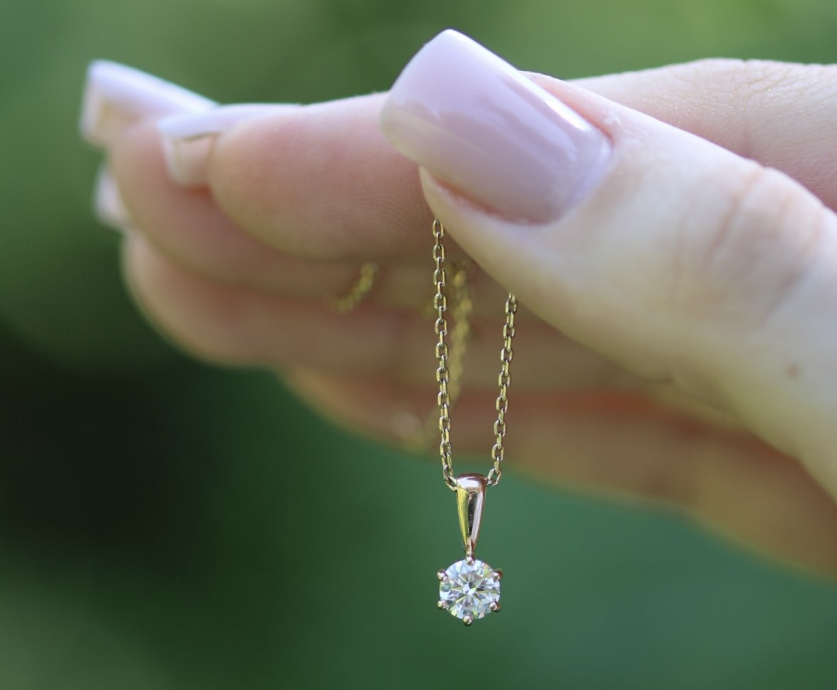 A hand holding a colorless round memorial diamond set in a necklace.