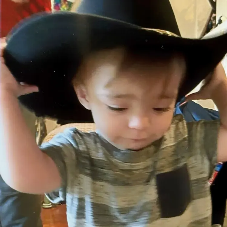 A little boy, putting on a big cowboy hat.