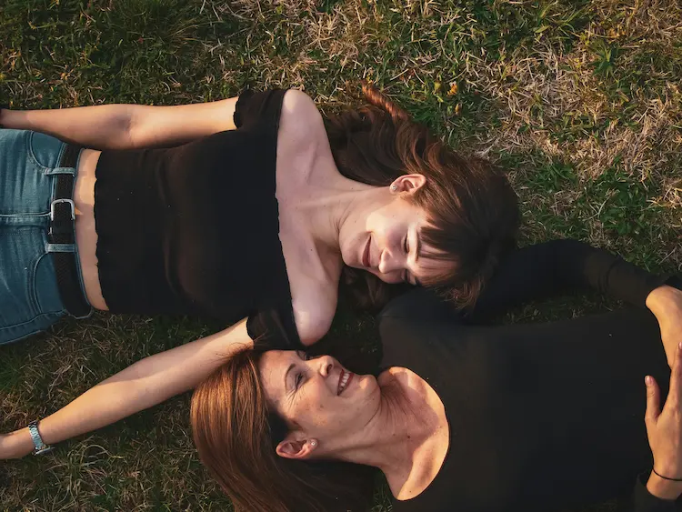 Mom and daughter, laying in the grass, looking at each other.