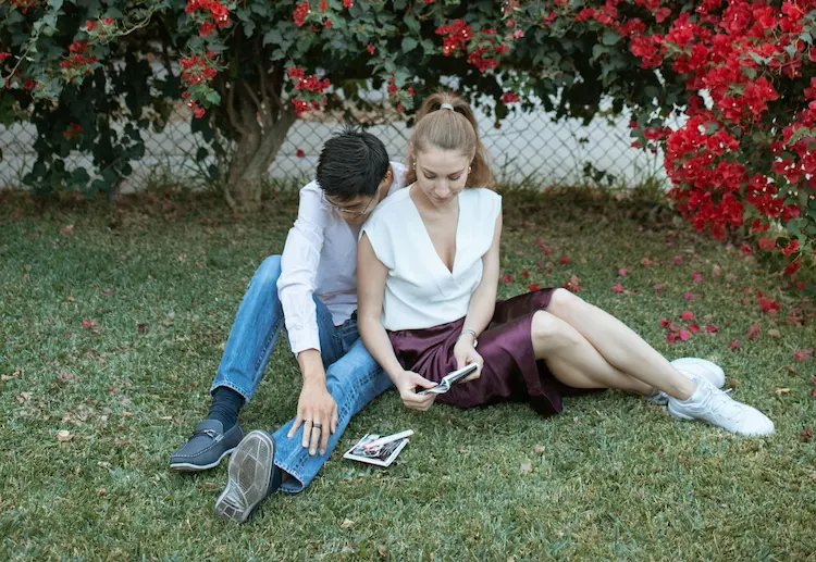 A girl and a boy, sitting on the grass, looking at pictures.