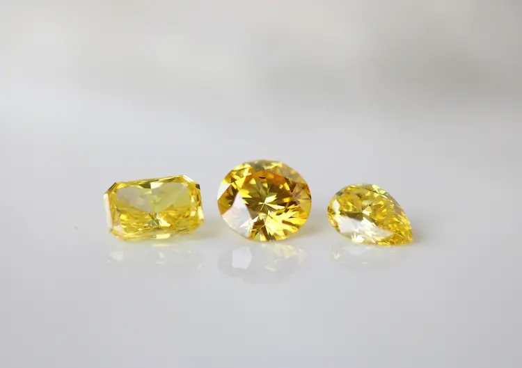 From left to right: a yellow radiant cut cremation diamond, a yellow round cut cremation diamond, and a yellow pear cut cremation diamond.