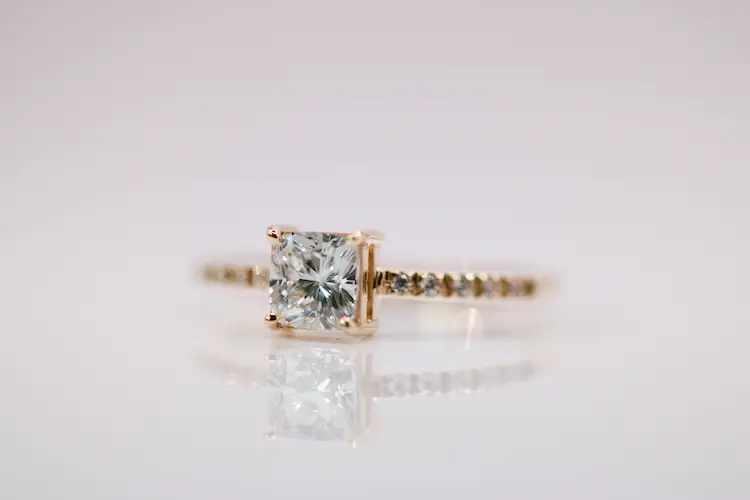 A colorless princess cut diamond in a yellow gold ring.