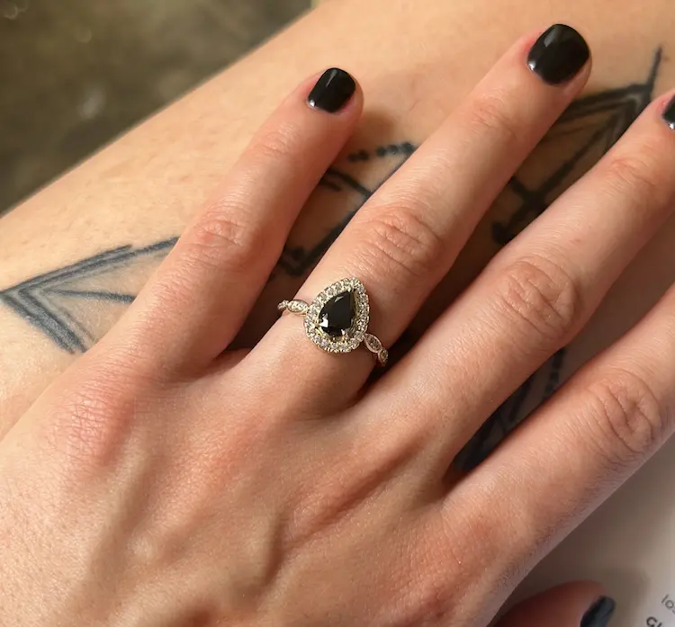 A woman's hand with a black pear cut memorial diamond engagement ring on her ring finger.