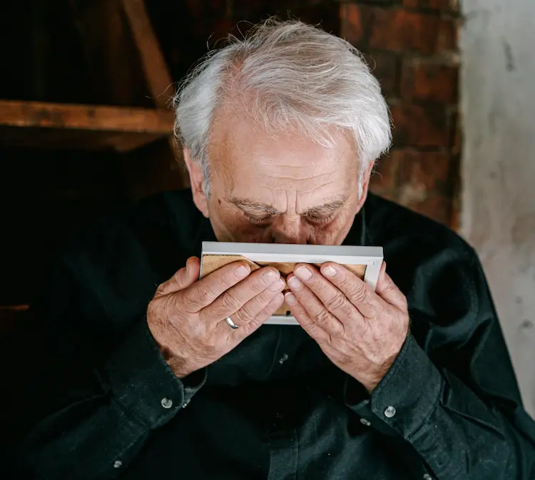 An older man kissing a photo.